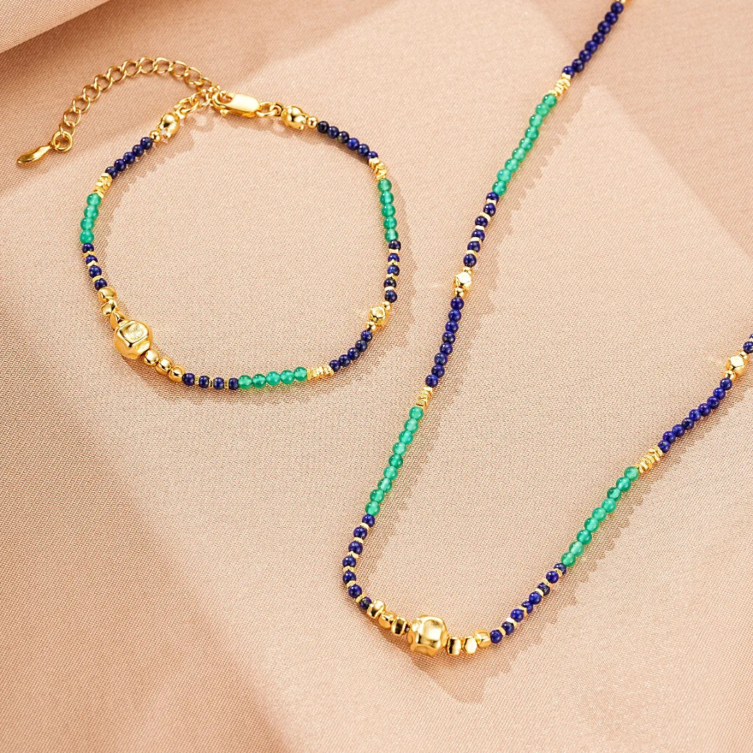 Ensemble de collier et bracelet en argent doré, ornés de perles de lapis-lazuli bleu foncé, de perles de jade vert émeraude et de perles dorées, avec une perle centrale dorée plus grande.