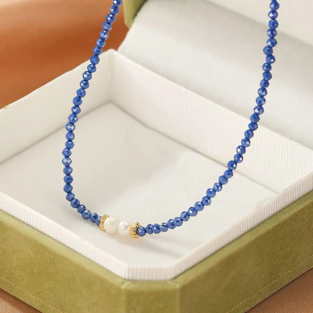 Collier "Délicatesse" en lapis lazuli bleu faceté et perles blanches, accents dorés, présenté dans une boîte écrin verte.