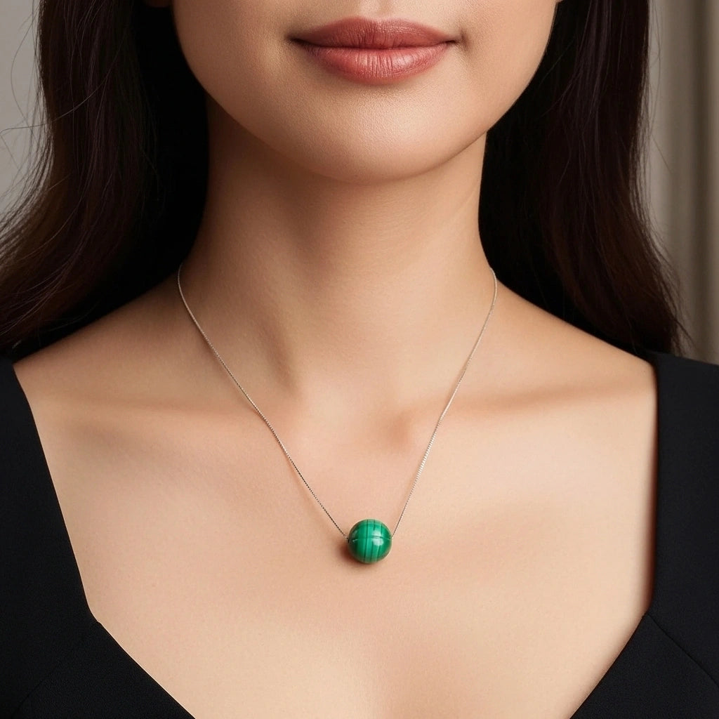 Collier en argent avec une perle ronde de malachite verte au centre, porté par une femme.
