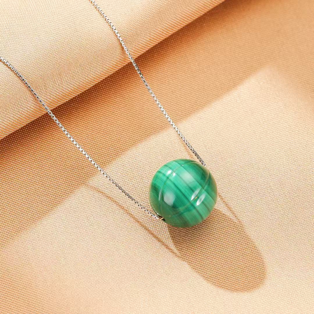 Collier "Beauté Naturelle" en argent avec une bille de malachite verte striée, sur un fond beige texturé.