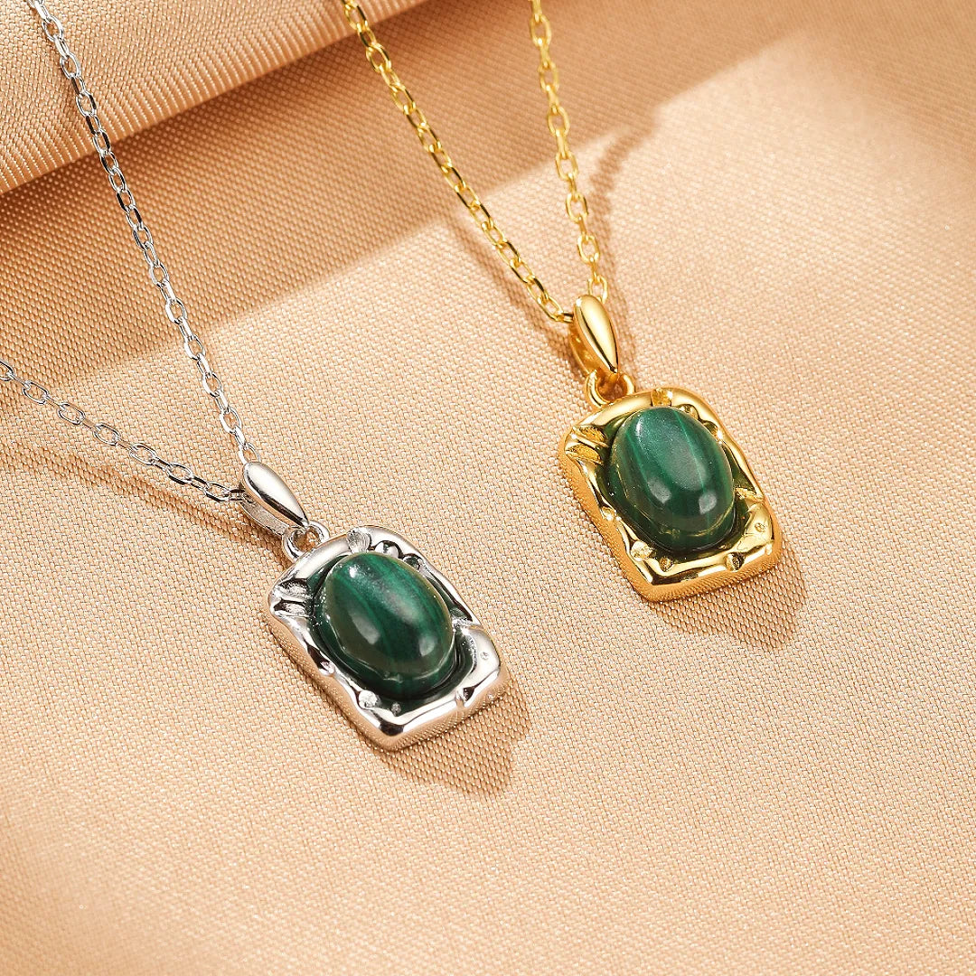 Collier "Élégance Intemporelle" en argent avec pendentif ovale en malachite verte facettée, présenté sur un fond beige texturé.