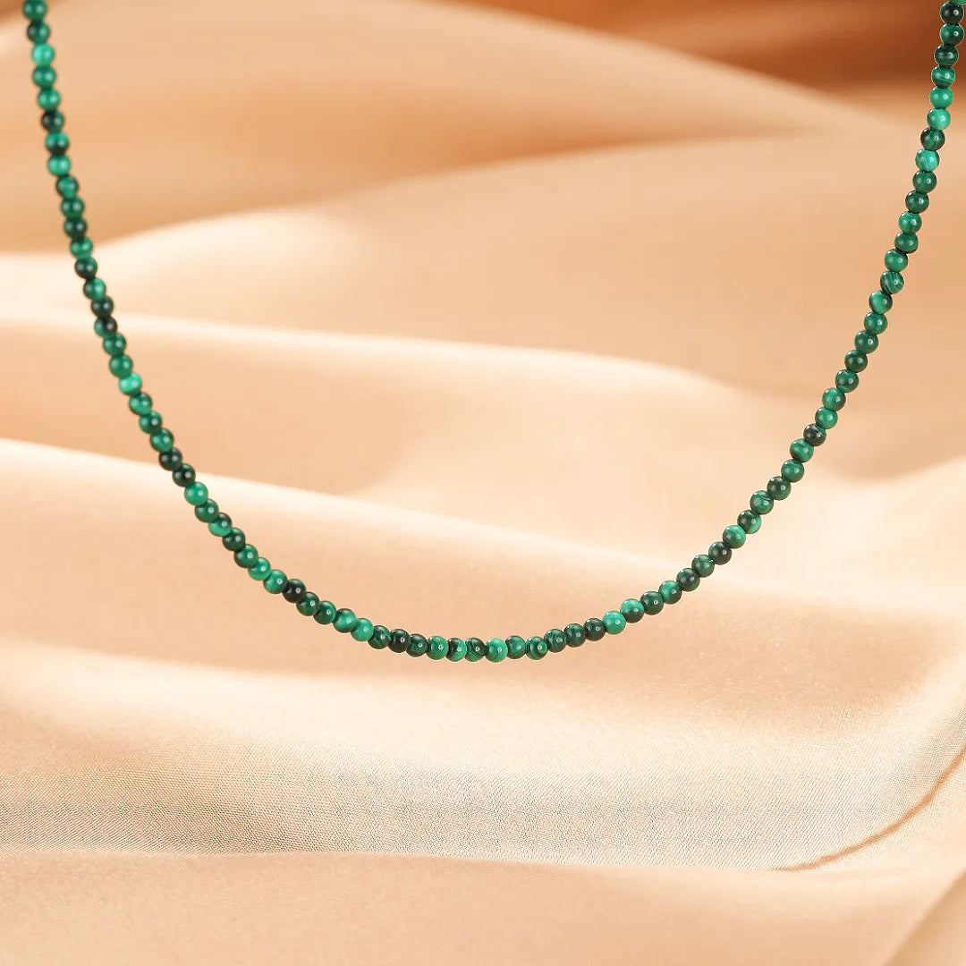 Collier fin en argent orné de petites perles rondes de malachite verte naturelle, sur fond satiné beige.