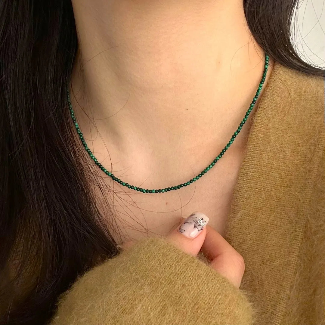 Collier fin en malachite naturelle et argent, porté par une femme avec un pull en laine marron.