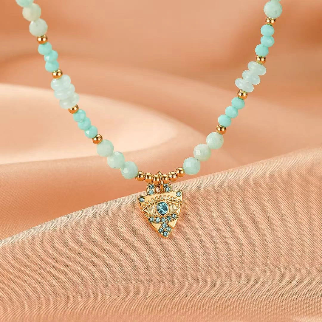 Collier "Œil Apaisant" avec perles d'amazonite et turquoise, orné d'un pendentif œil bleu stylisé en forme de bouclier avec des cristaux.