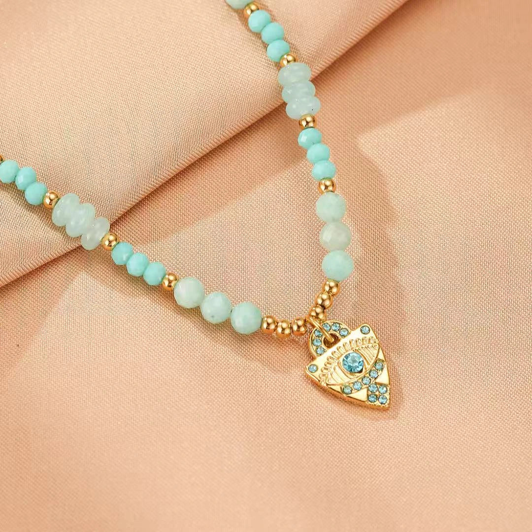 Collier "Œil Apaisant" avec pendentif mauvais œil doré serti de cristaux bleus et perles d'amazonite bleu pâle.