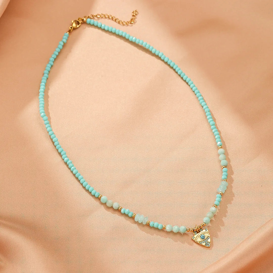 Collier "Œil Apaisant" avec perles bleu turquoise, amazonite, petites perles dorées et un pendentif triangulaire doré serti d'un œil bleu.