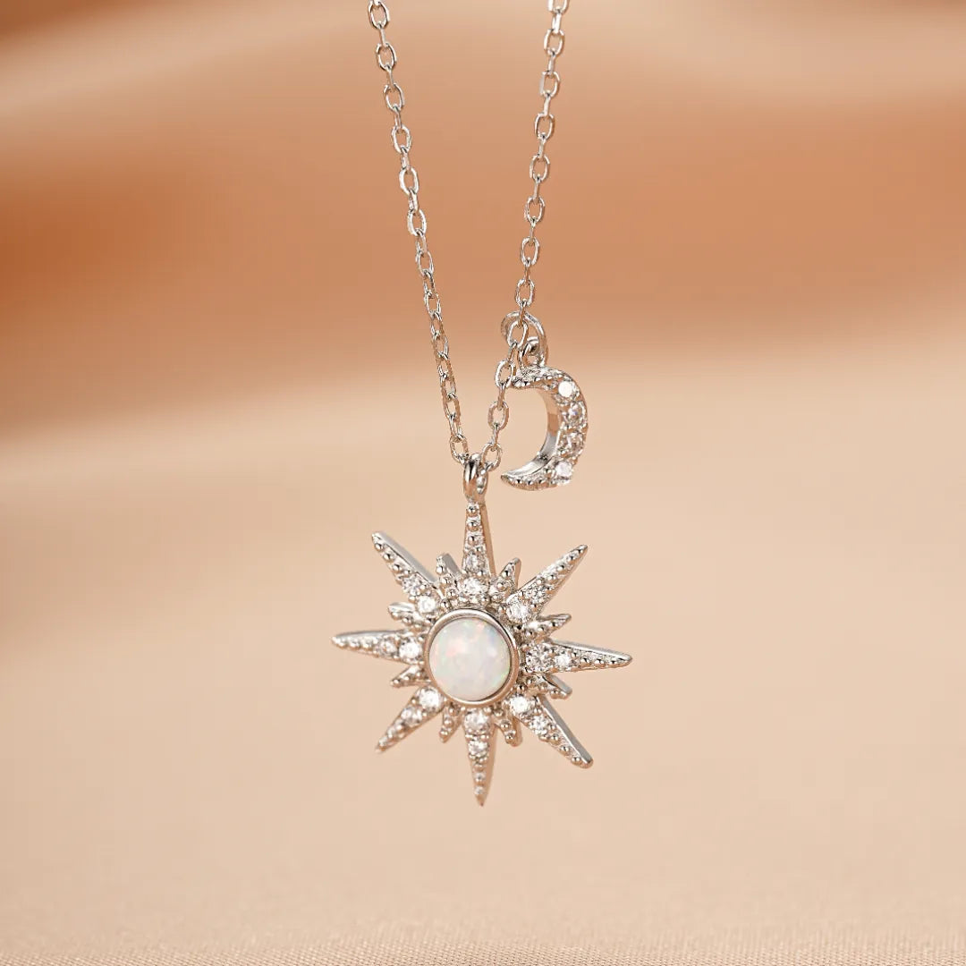Collier en argent avec un pendentif en forme d'étoile orné d'une opale blanche et de petits cristaux, suspendu à une fine chaîne, avec une petite lune scintillante comme breloque.
