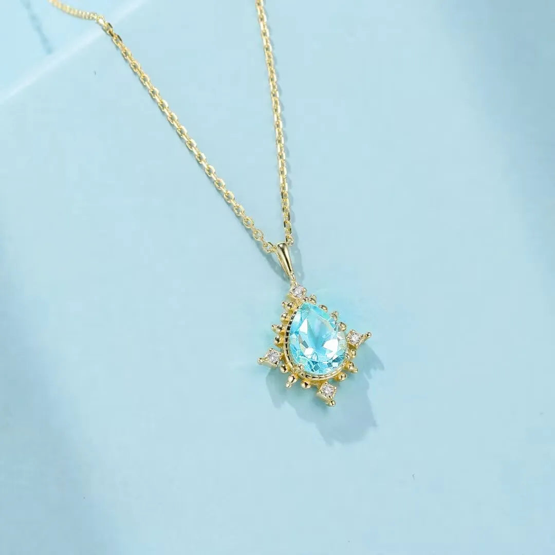 Collier en argent 925 avec une topaze bleue en forme de poire et des petits diamants incrustés, le tout monté sur une chaîne dorée.