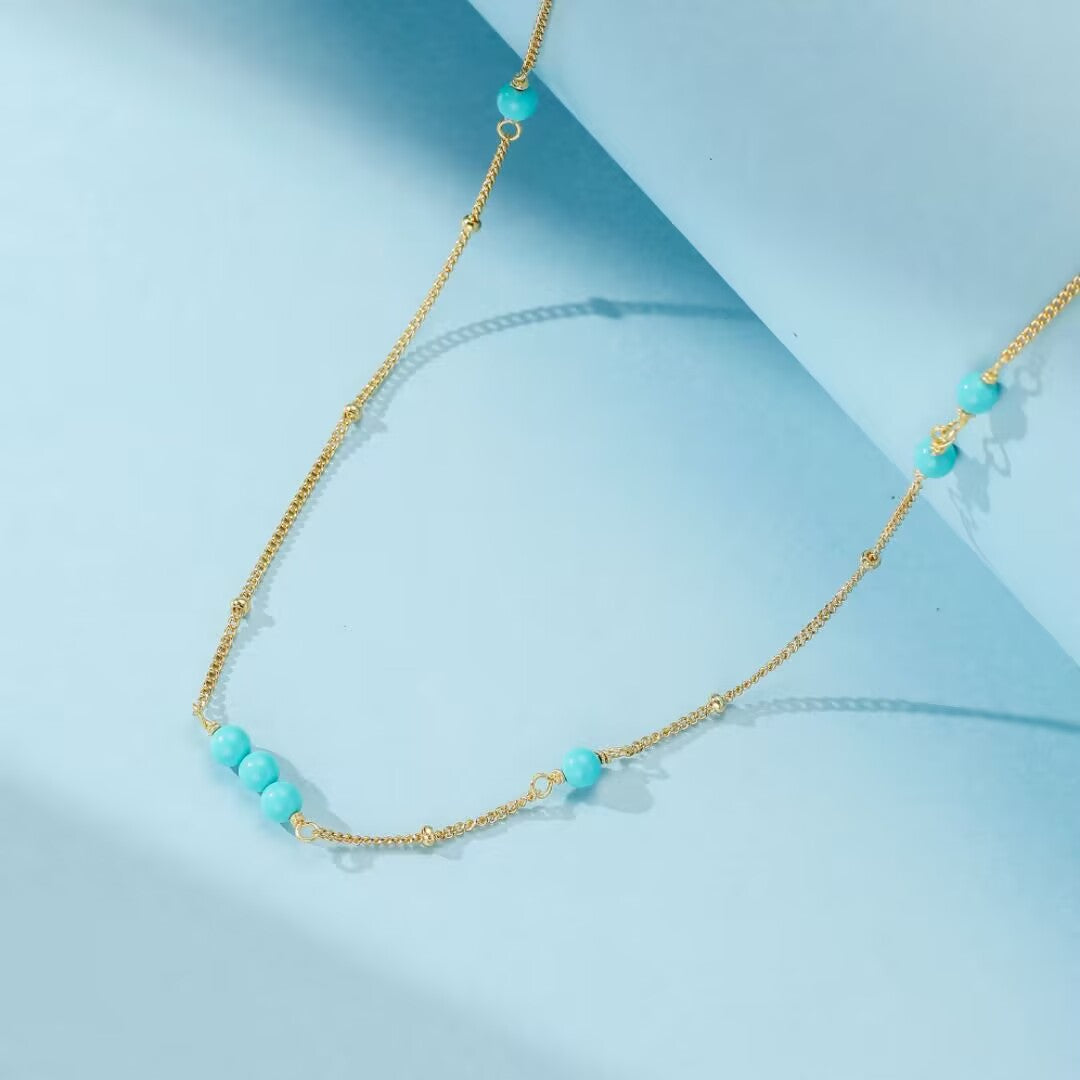 Collier "Dunes de Charme" en argent doré or, avec une chaîne fine ponctuée de perles turquoise bleues.
