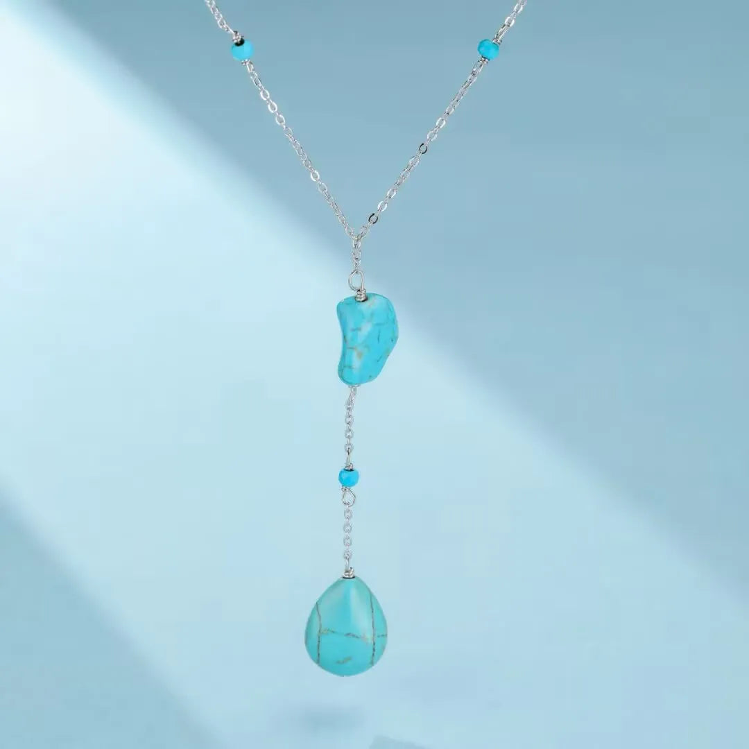 Collier "Voyage Céleste" en argent avec une pierre turquoise brute en forme de croissant et une pierre turquoise polie en forme de goutte, orné de petites perles turquoise.