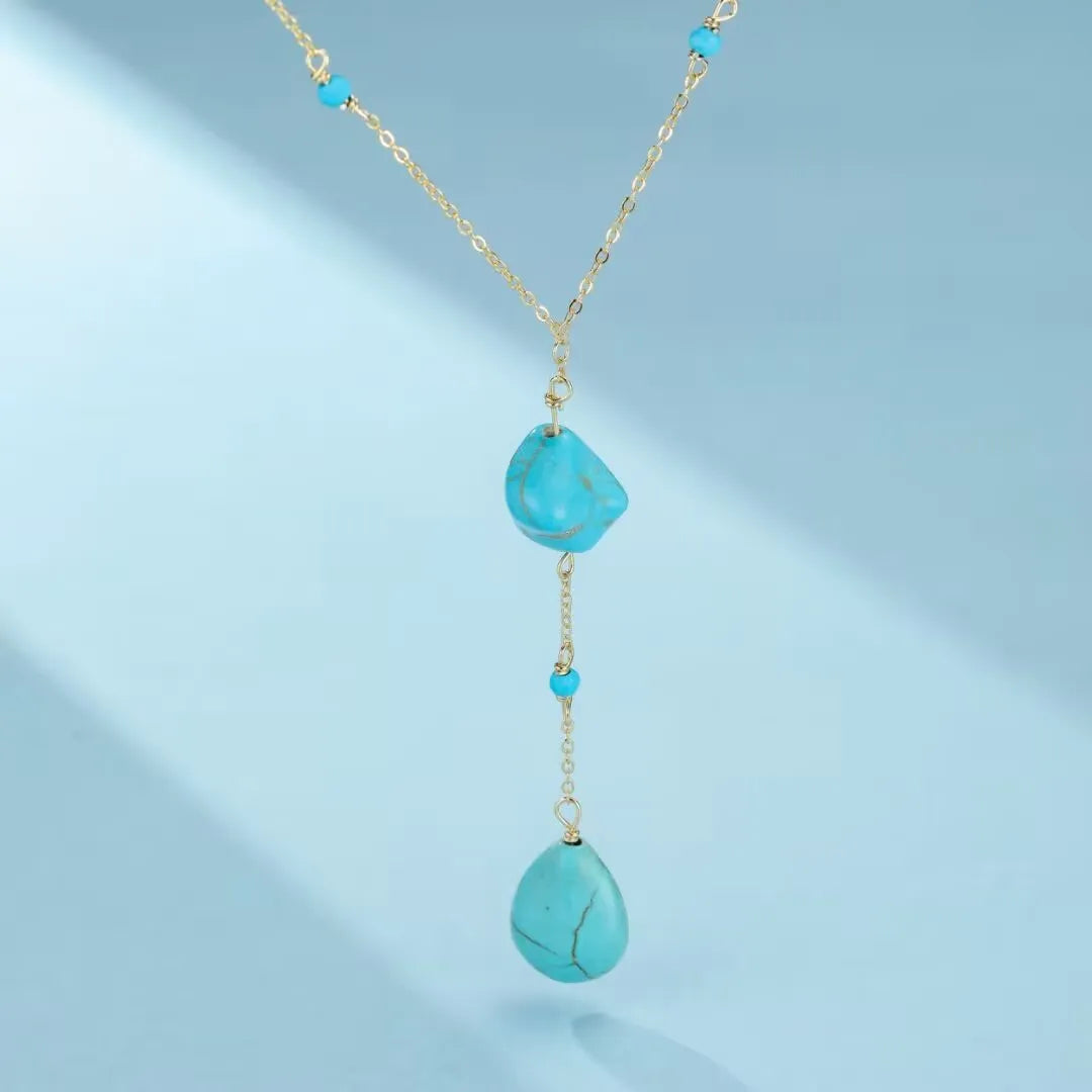 Collier "Voyage Céleste" en argent avec deux pendentifs en turquoise brute et des petites perles turquoises sur une chaîne dorée.