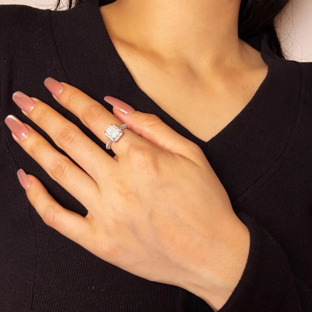 Bague opale "Reflet Royal" en argent, portée à l'annulaire d'une main aux ongles vernis en rose pâle.