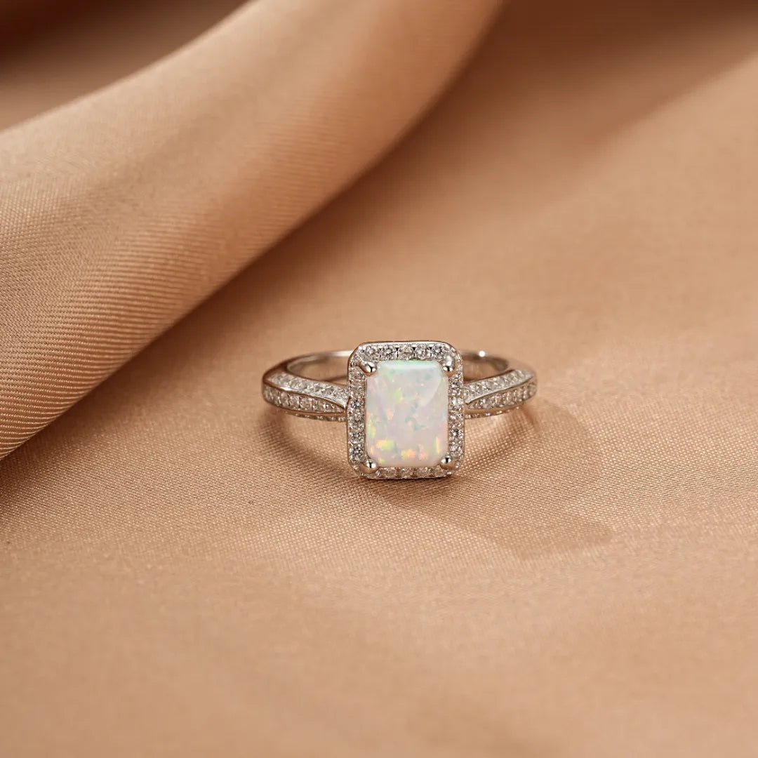 Bague en argent "Reflet Royal" ornée d'une opale rectangulaire centrale entourée de petits cristaux scintillants sur un fond satiné.