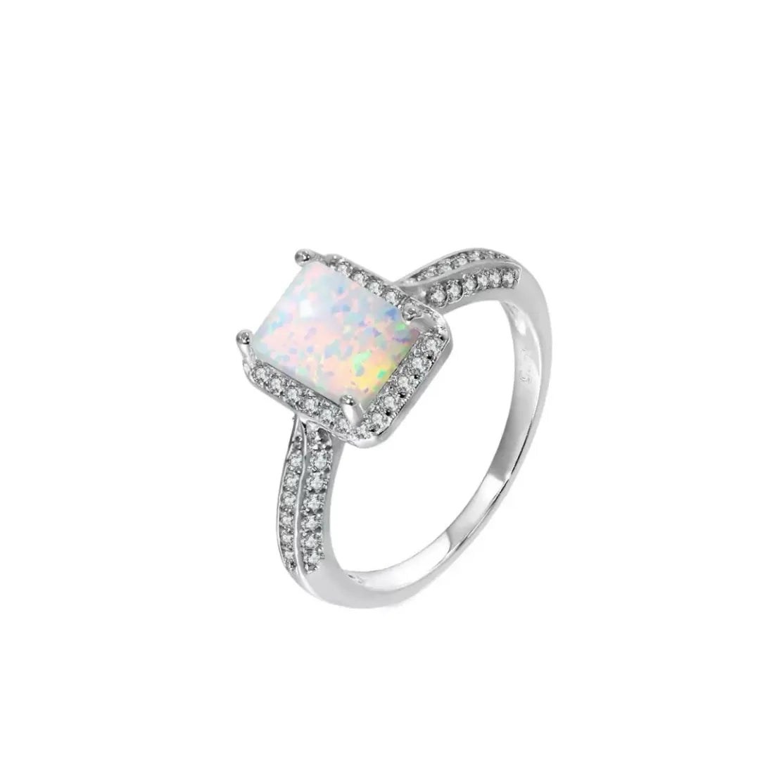 Bague en argent avec une opale carrée centrale entourée de petites pierres scintillantes et une monture ornée de cristaux.