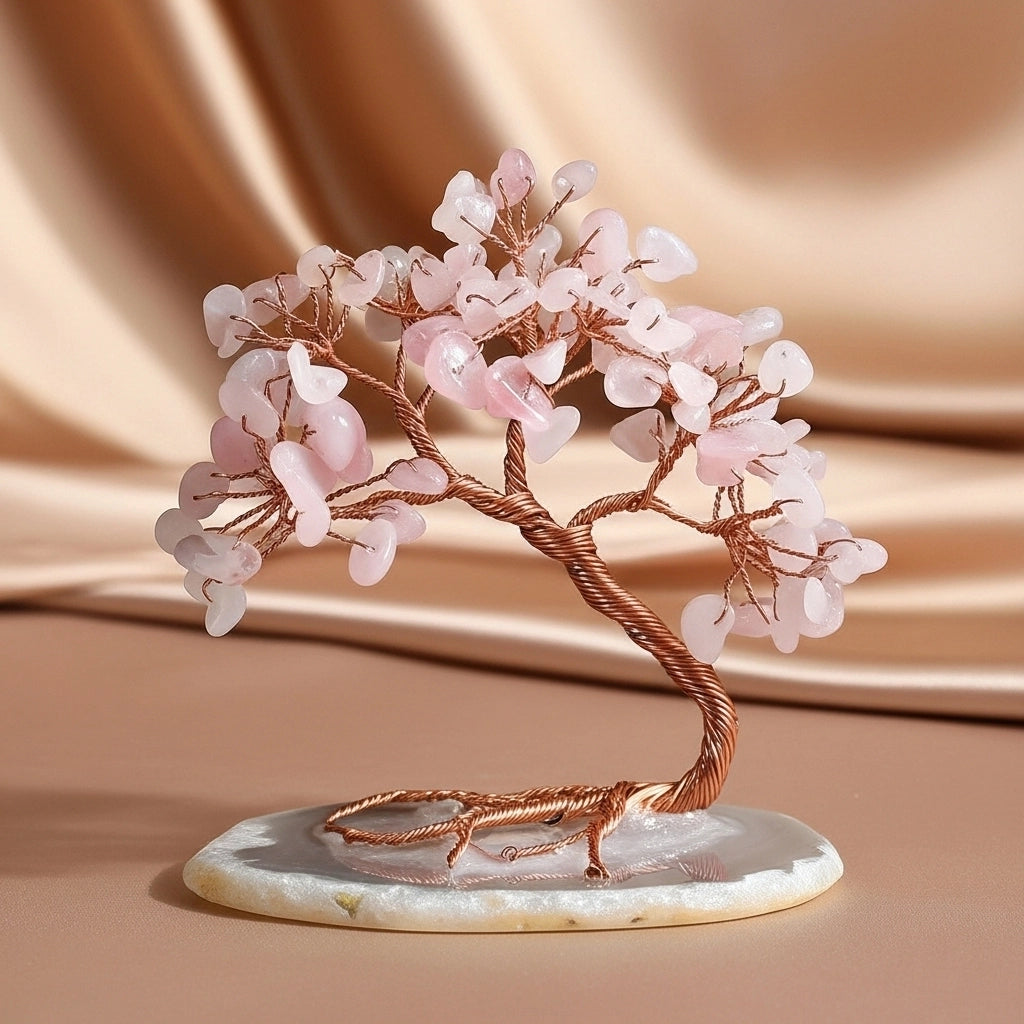 Arbre de vie décoratif en quartz rose avec des feuilles en pierres roses et un tronc en fil de cuivre torsadé, reposant sur une base en agate polie.