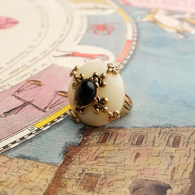 Bague Agate Noire "Pureté Mystique" avec un cabochon central noir entouré de détails dorés sur une surface illustrée de cartes astrologiques.
