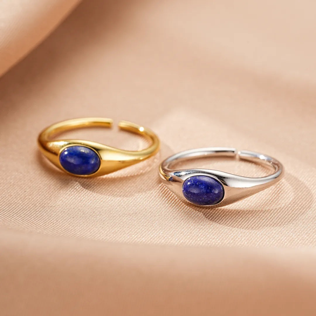 Bague en argent plaqué or avec une pierre de lapis-lazuli ovale et une bague en argent avec une pierre de lapis-lazuli ovale, sur un fond en tissu beige.