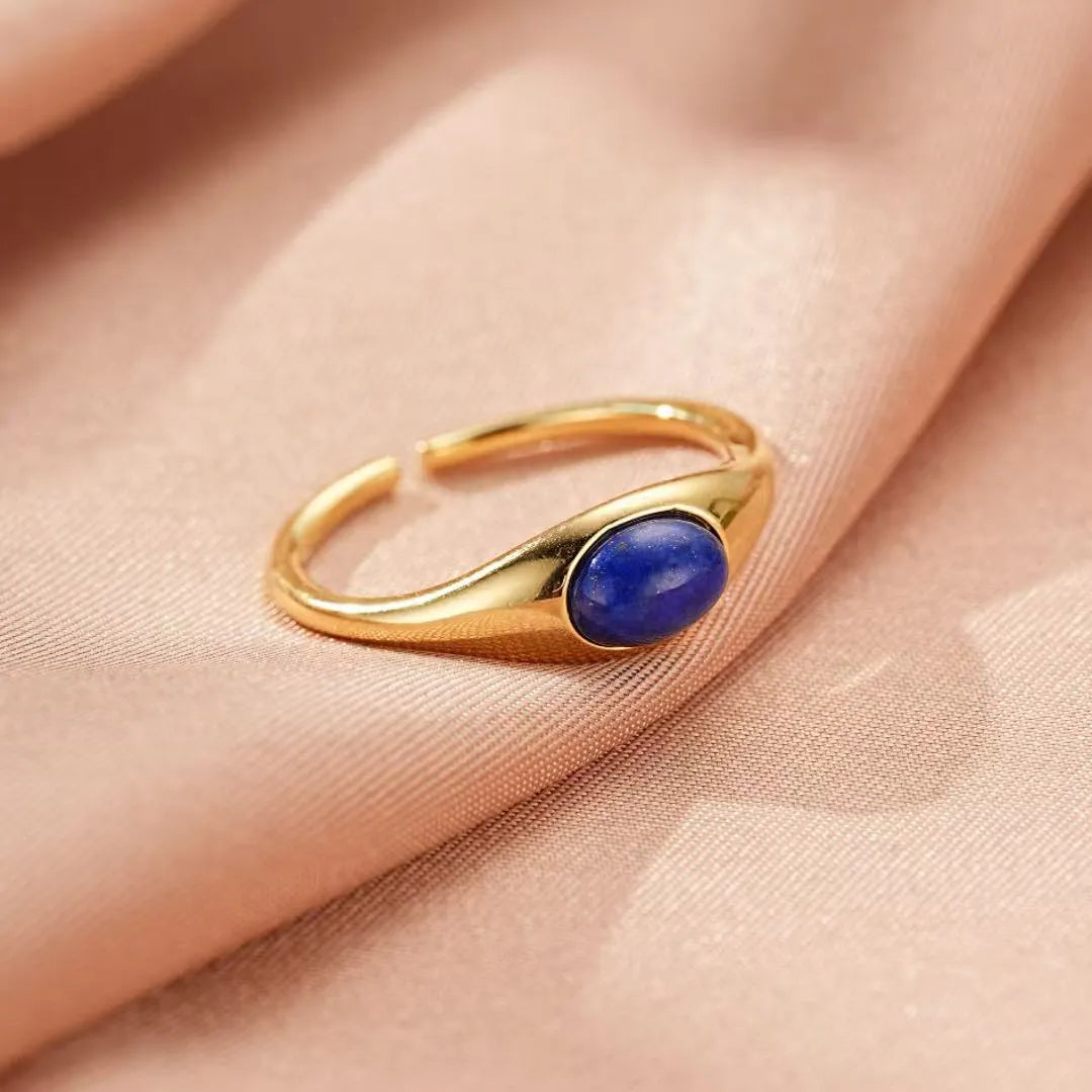 Bague ajustable en argent plaqué or avec une pierre de lapis-lazuli ovale bleue sur un fond de tissu rose satiné.
