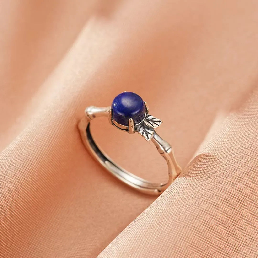 Bague en argent avec une pierre de lapis lazuli bleu profond, design inspiré de la nature avec des feuilles et une tige rappelant le bambou.
