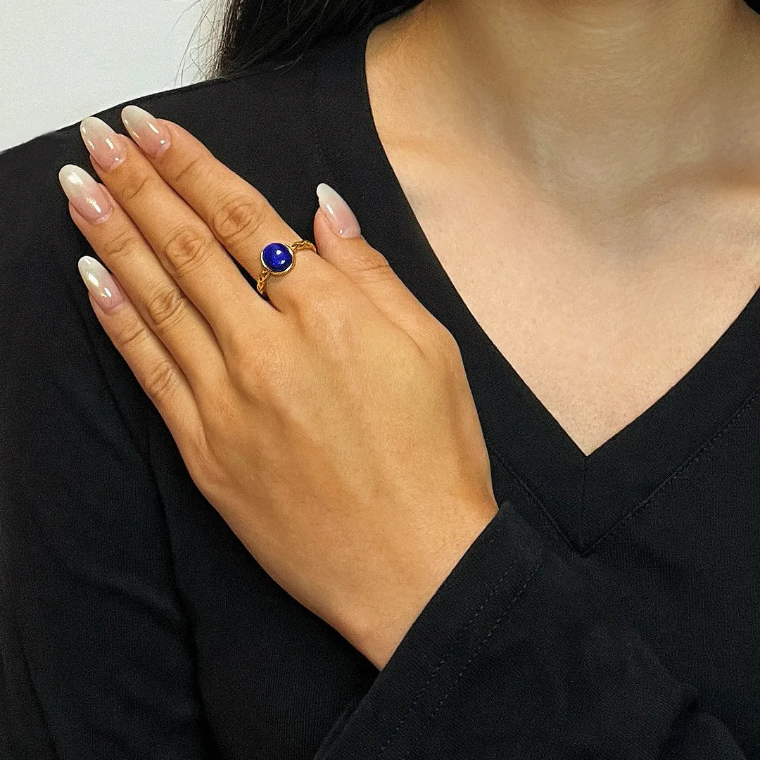 Bague en argent doré or 18K avec un cabochon rond de lapis-lazuli bleu profond, portée à l'annulaire gauche d'une femme.