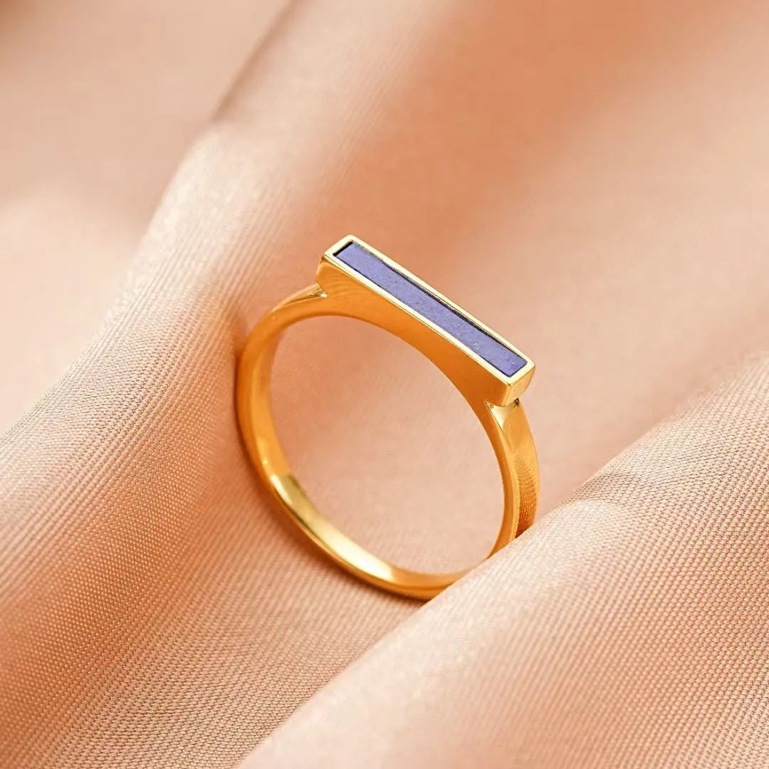 Bague fine en argent doré avec une barre rectangulaire bleue incrustée de lapis-lazuli, posée sur un tissu satiné rose.