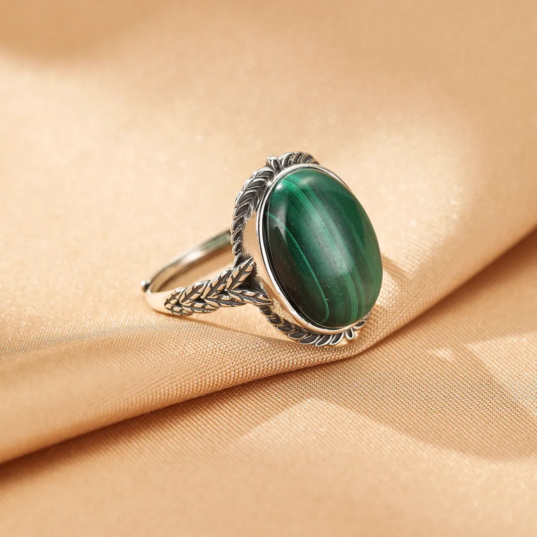 Bague en argent avec une grosse pierre ovale de malachite verte aux motifs concentriques, sertie sur un anneau orné de détails végétaux stylisés.