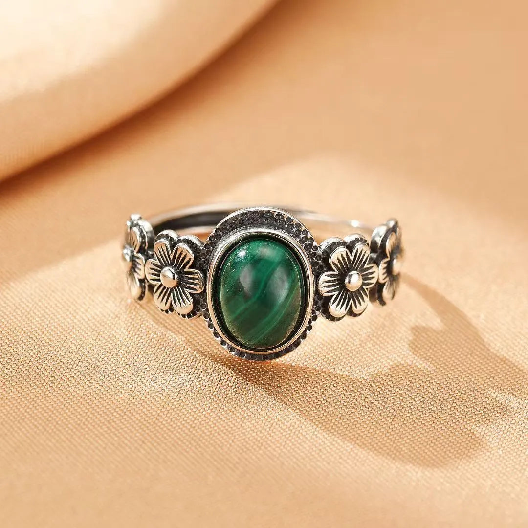 Bague en argent ornée d'une pierre de malachite centrale ovale et de motifs floraux tout autour de l'anneau.