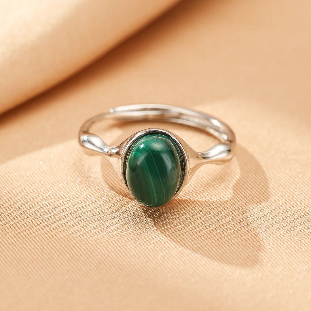 Bague en argent avec une pierre de malachite ovale et verte, sertie sur un anneau fin. La malachite présente des bandes naturelles distinctes.