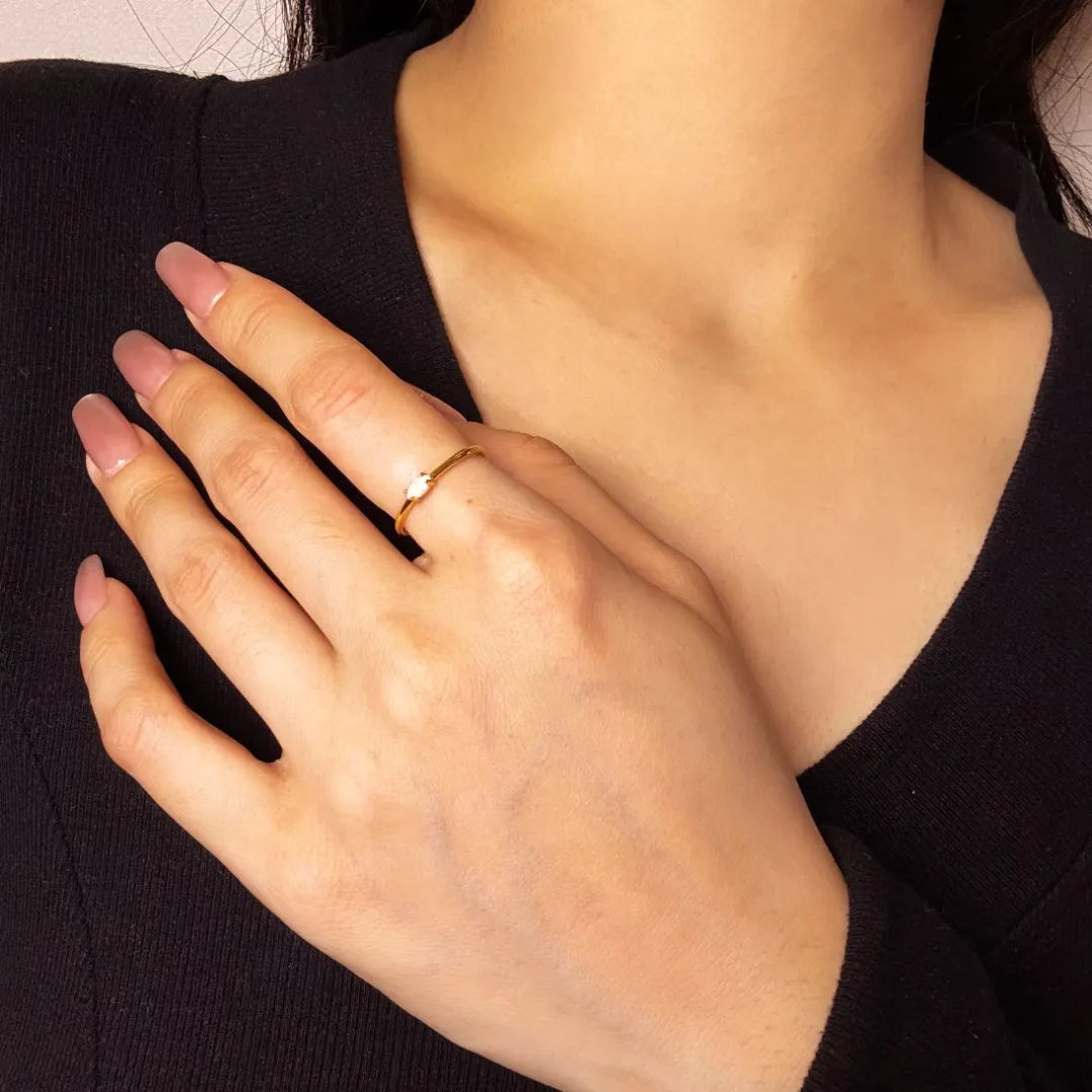 Bague fine en argent doré or avec une opale blanche sur le doigt d'une femme