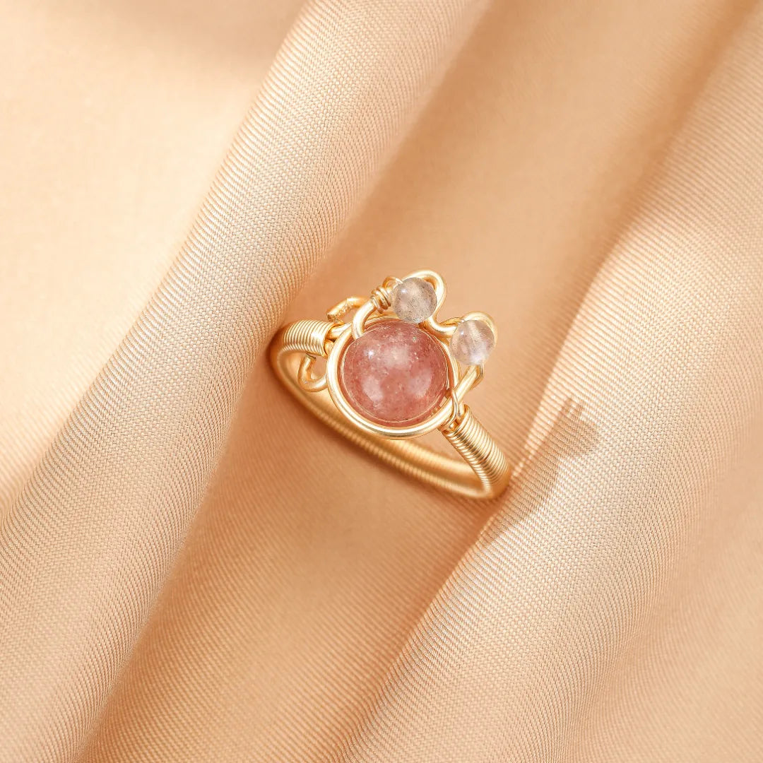 Bague en or 14 carats sertie d'une pierre naturelle rose et de deux petites pierres claires, design filigrane rappelant un chaton joyeux.