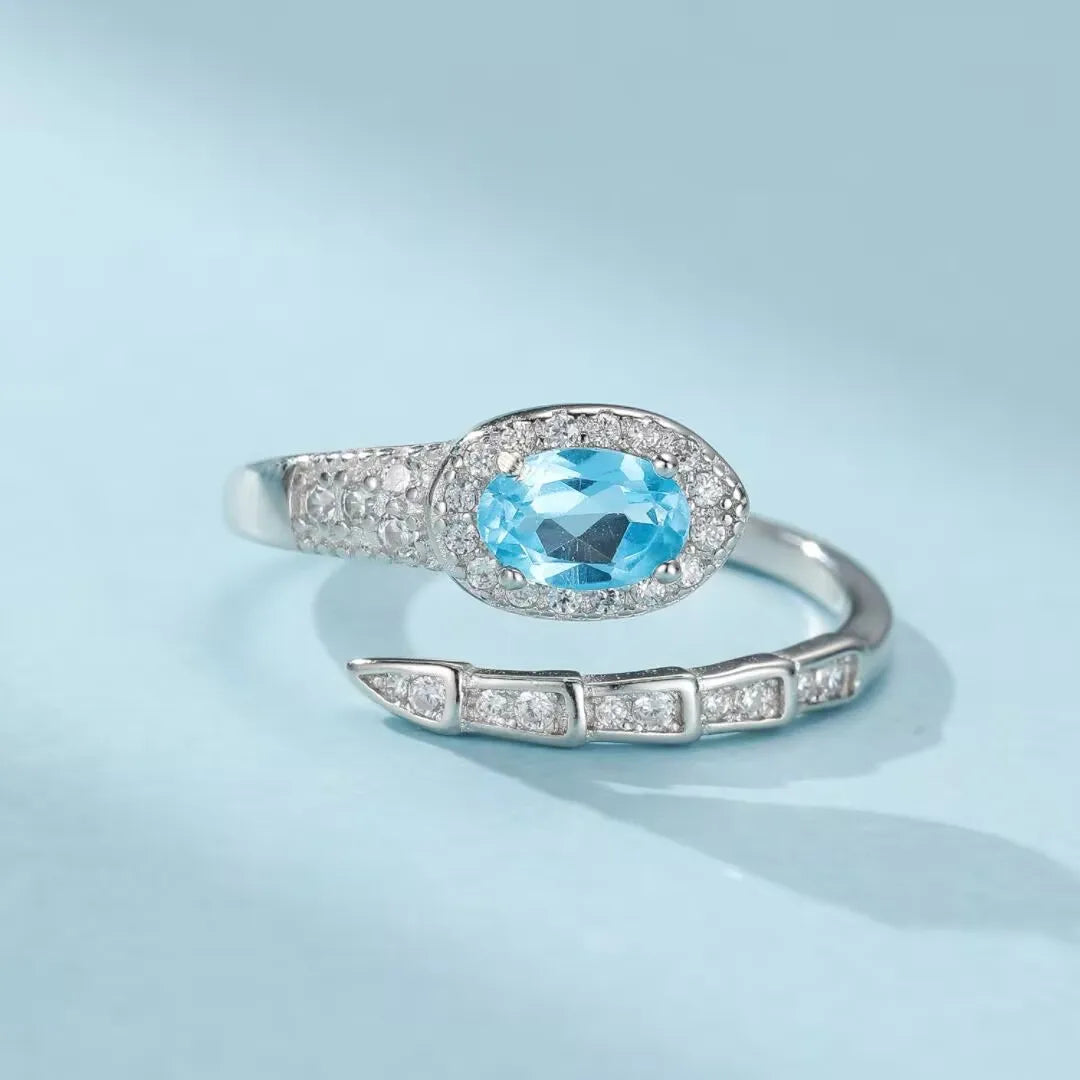Bague serpent en argent 925 ornée d'une topaze bleue ovale entourée de zirconiums blancs scintillants, la queue du serpent est également sertie de petits zirconiums.