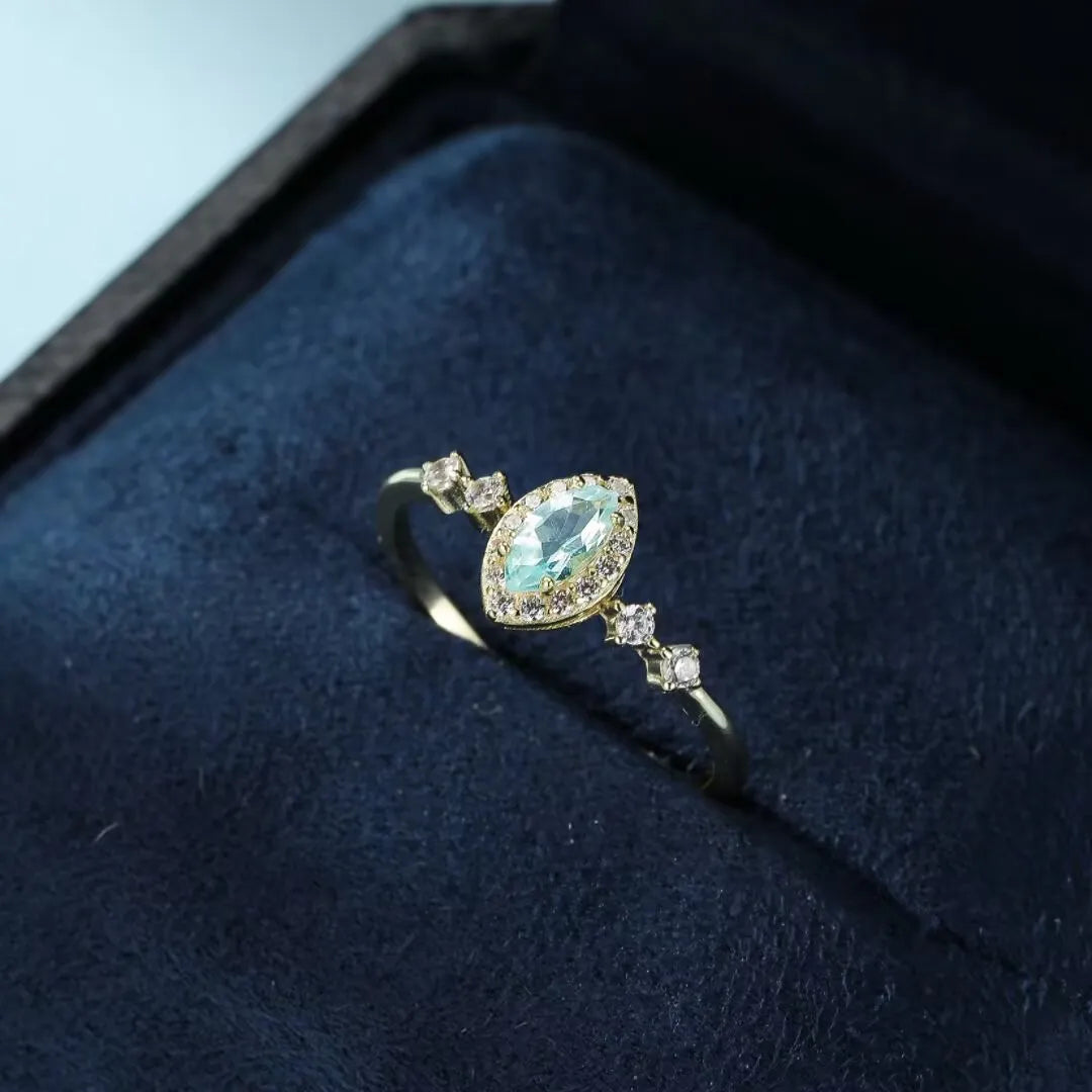 Bague en argent 925 sertie d'une topaze bleu clair ovale entourée de petits diamants scintillants, sur un écrin bleu.