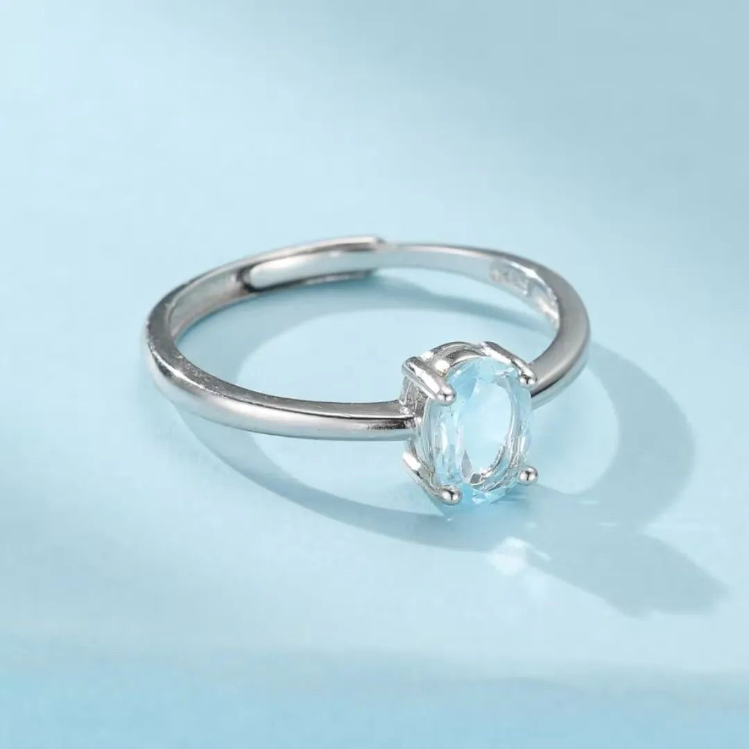 Bague en argent 925 ajustable avec une topaze bleue ovale "Élégance Pure" sur fond bleu ciel.