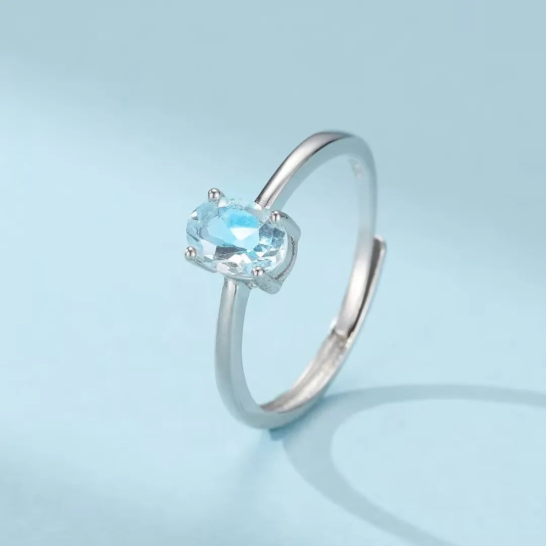 Bague en argent 925 avec une topaze bleue ovale facetée, style minimaliste et ajustable, nommée "Élégance Pure".