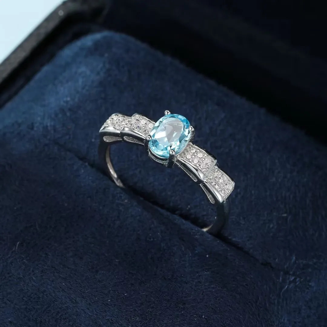 Bague en argent 925 ornée d'une topaze bleue ovale et de petits cristaux scintillants formant un motif de nœud papillon.