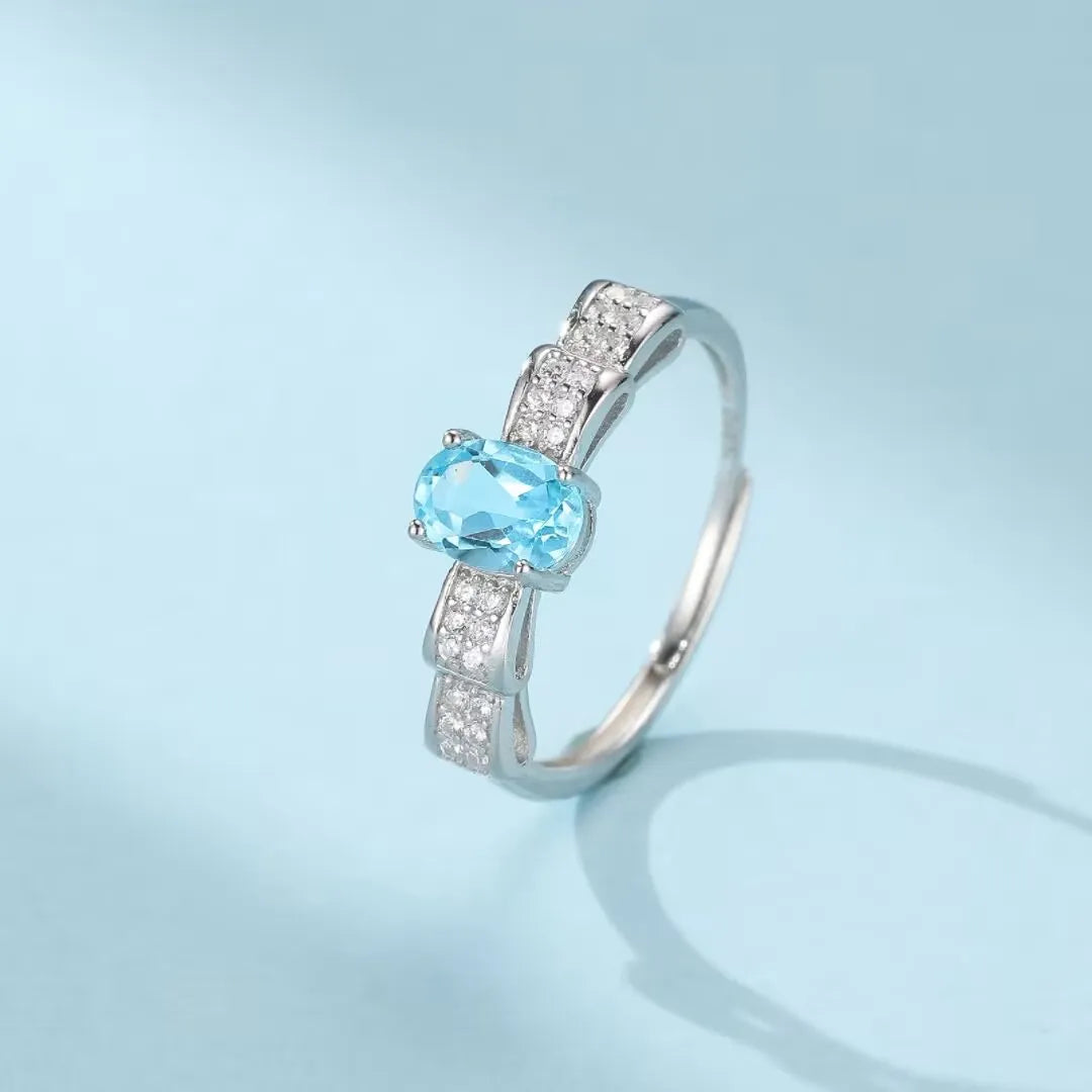 Bague en argent 925 ornée d'une topaze bleue ovale et de petits zirconiums blancs sertis sur un design en nœud papillon.