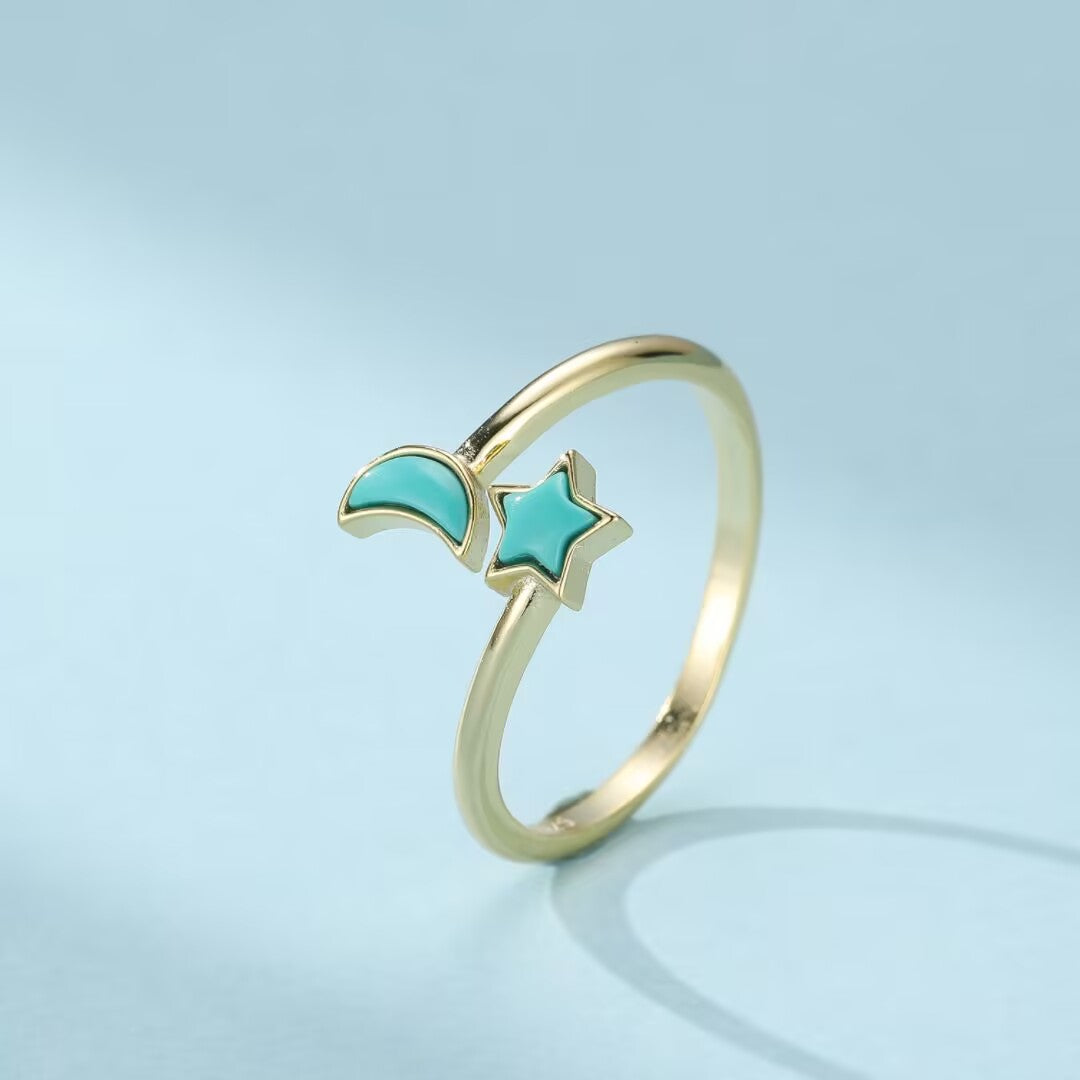 Bague ajustable en argent doré ornée d'une turquoise en forme d'étoile et d'un croissant de lune sur fond bleu clair.