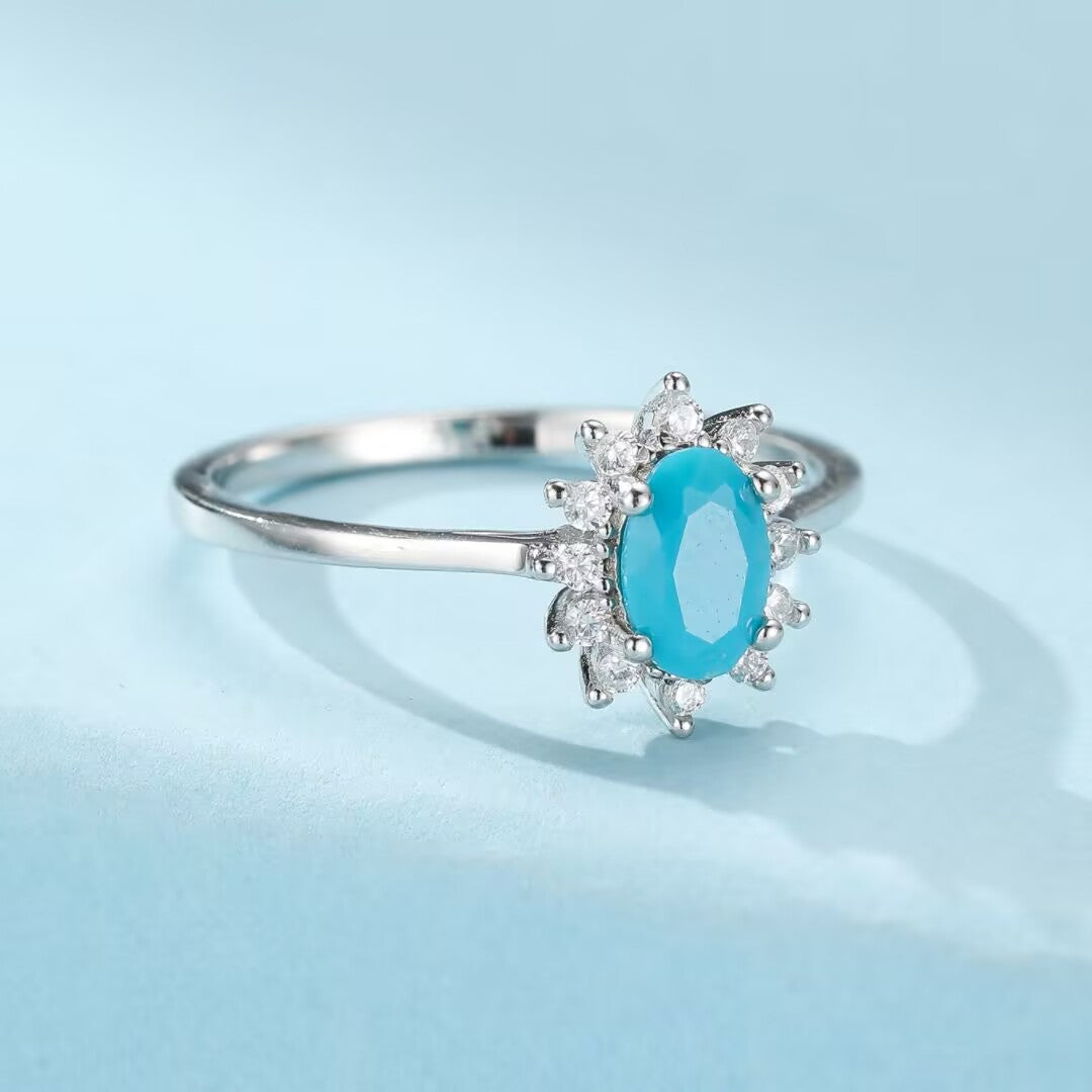 Bague en argent 925 ornée d'une turquoise ovale sertie en son centre, entourée de petites pierres blanches scintillantes formant une auréole florale.