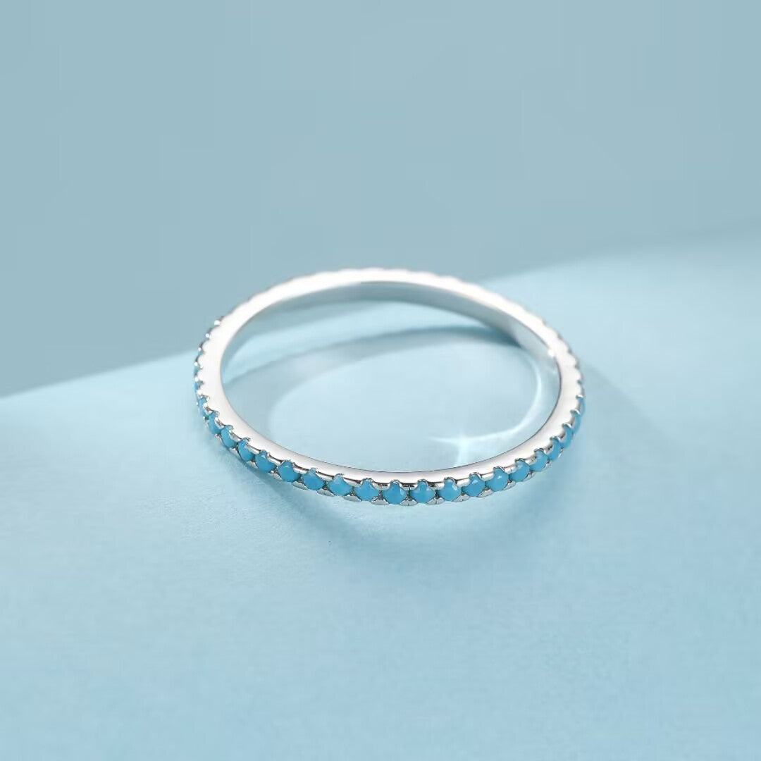 Bague fine en argent 925 sertie de nombreuses petites pierres turquoise bleues, posée sur un fond bleu clair.