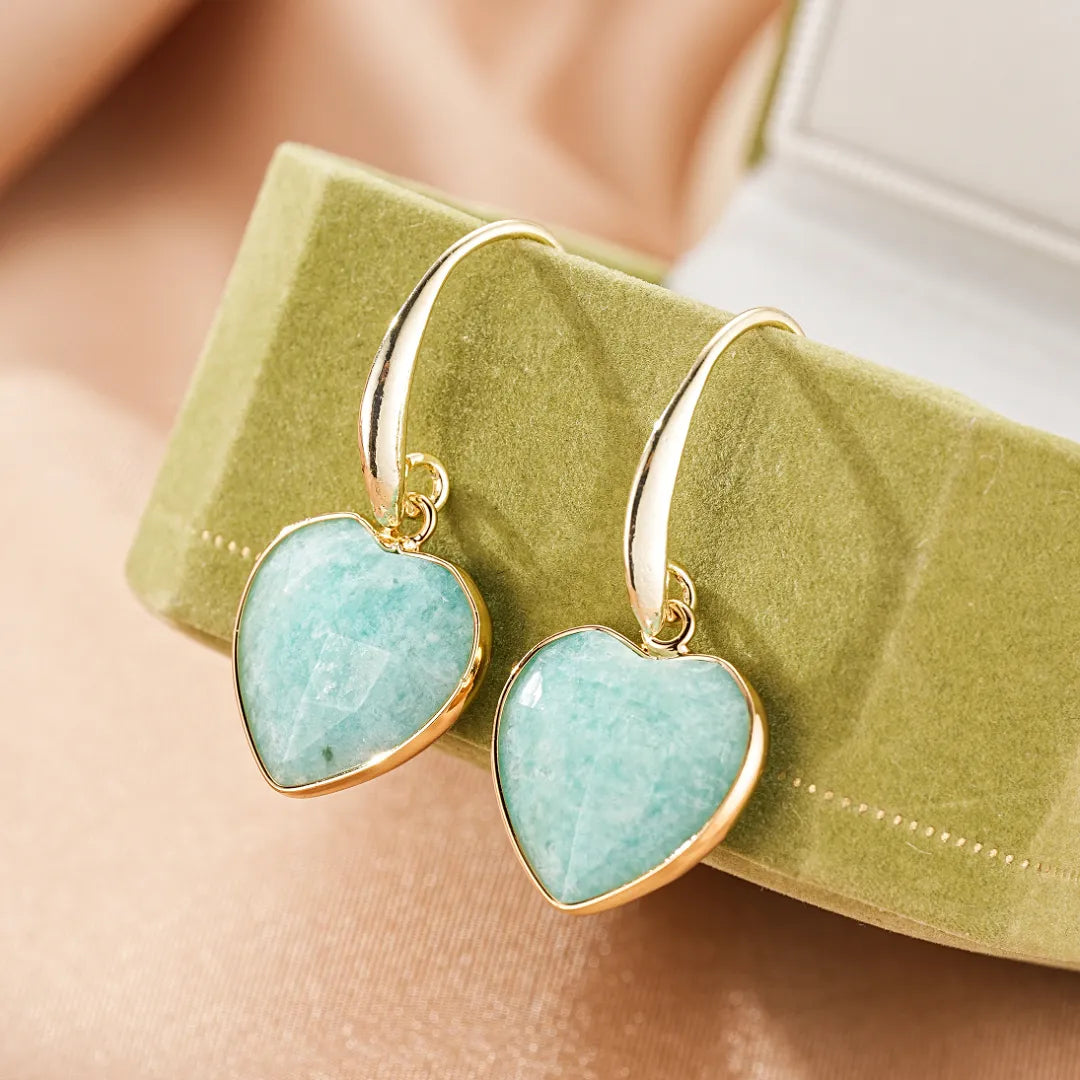 Boucles d'oreilles en forme de cœur en amazonite bleue avec monture dorée, présentées dans une boîte verte.