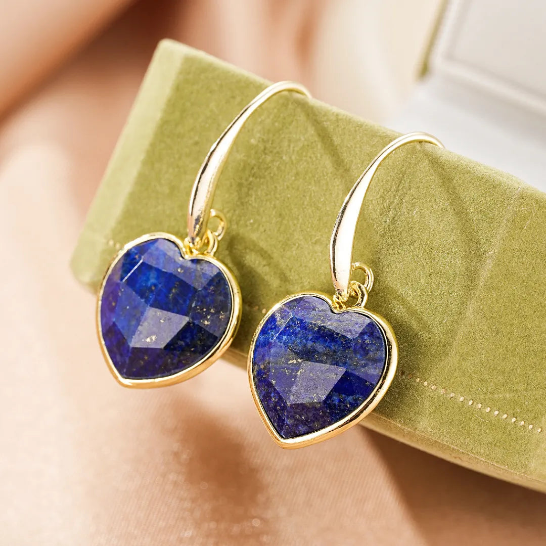 Boucles d'oreilles en forme de cœur en lapis-lazuli avec monture dorée, présentées sur un écrin vert.