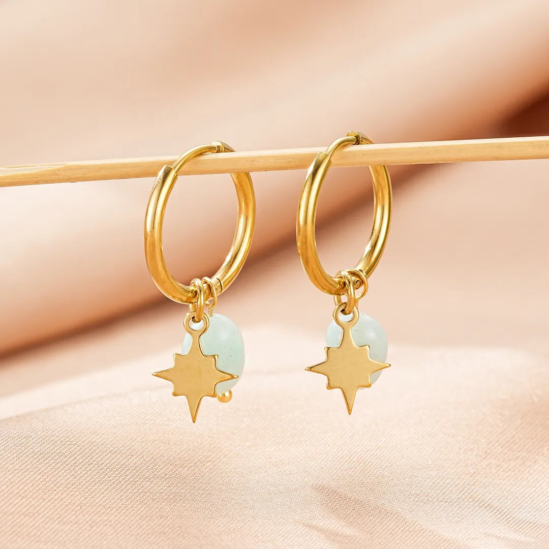 Paire de boucles d'oreilles créoles dorées ornées d'une petite pierre bleue pâle et d'un pendentif étoile dorée.