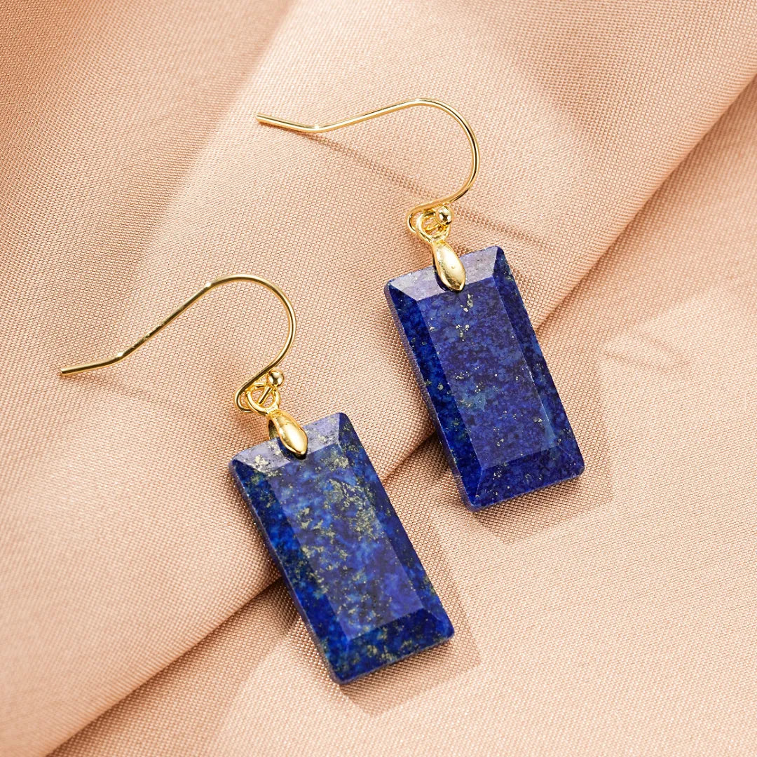 Boucles d'oreilles rectangulaires en lapis-lazuli avec fermoir en or, sur fond rose doux.