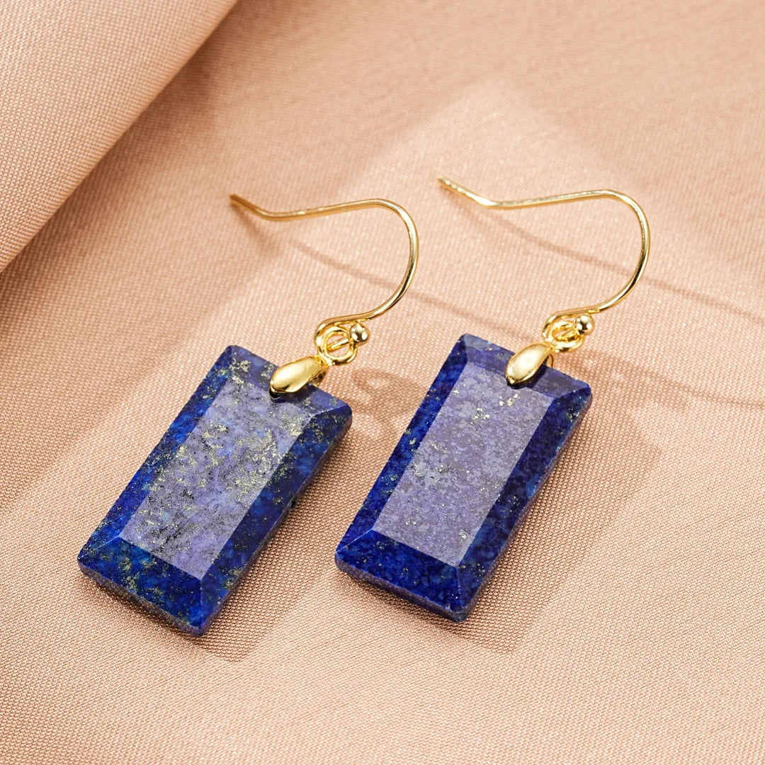 Paire de boucles d'oreilles rectangulaires en lapis-lazuli bleu profond avec des inclusions dorées, suspendues à des crochets dorés.