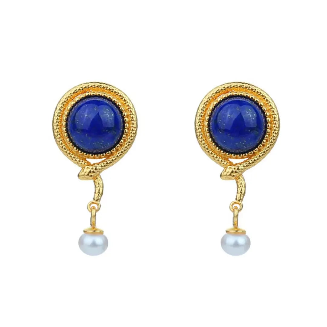 Boucles d'oreilles serpent en argent doré ornées d'un cabochon rond en lapis lazuli et d'une petite perle blanche suspendue.
