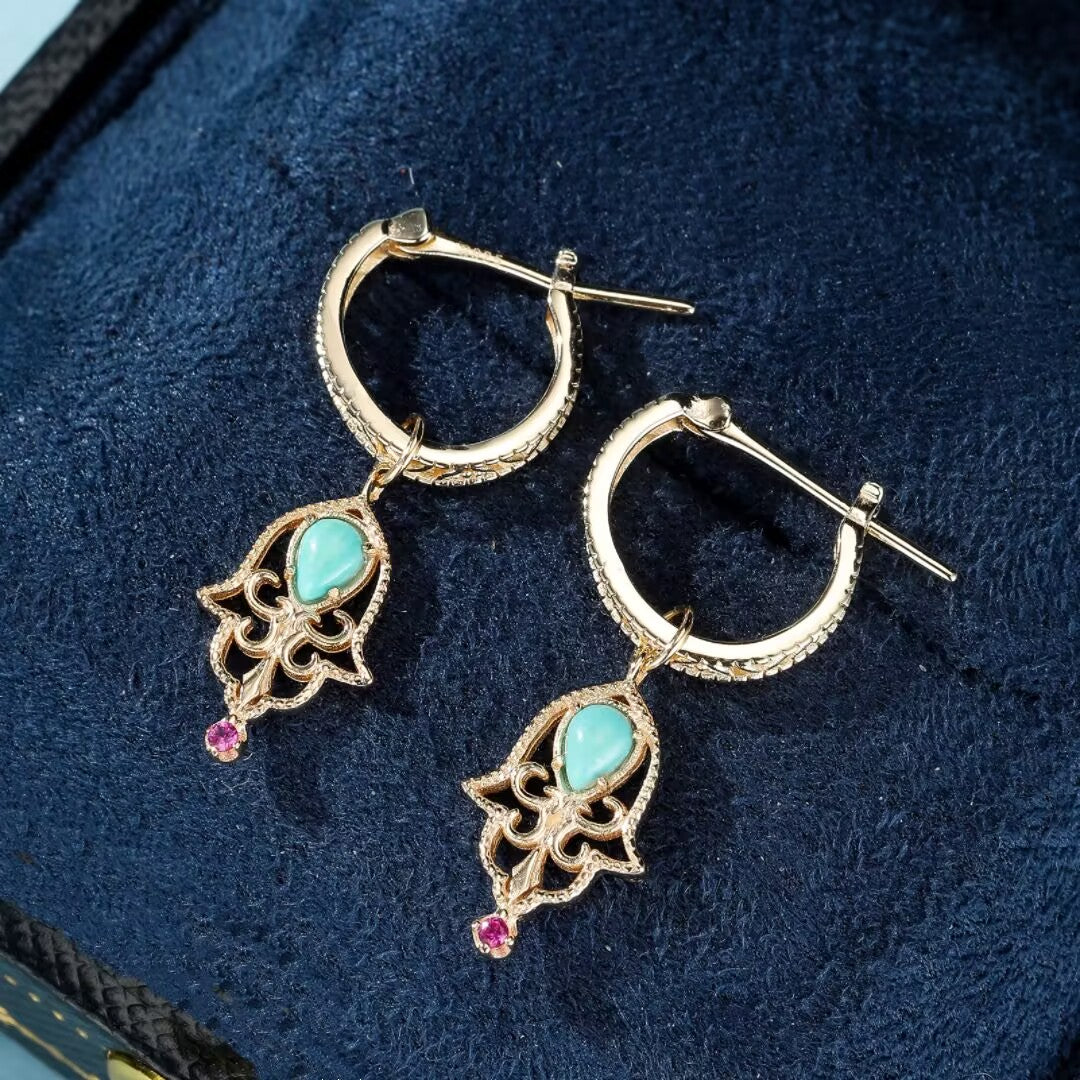 Boucles d’oreilles pendantes en argent doré ornées de turquoise et d'une petite pierre rose, inspirées du design de la main de Fatma.