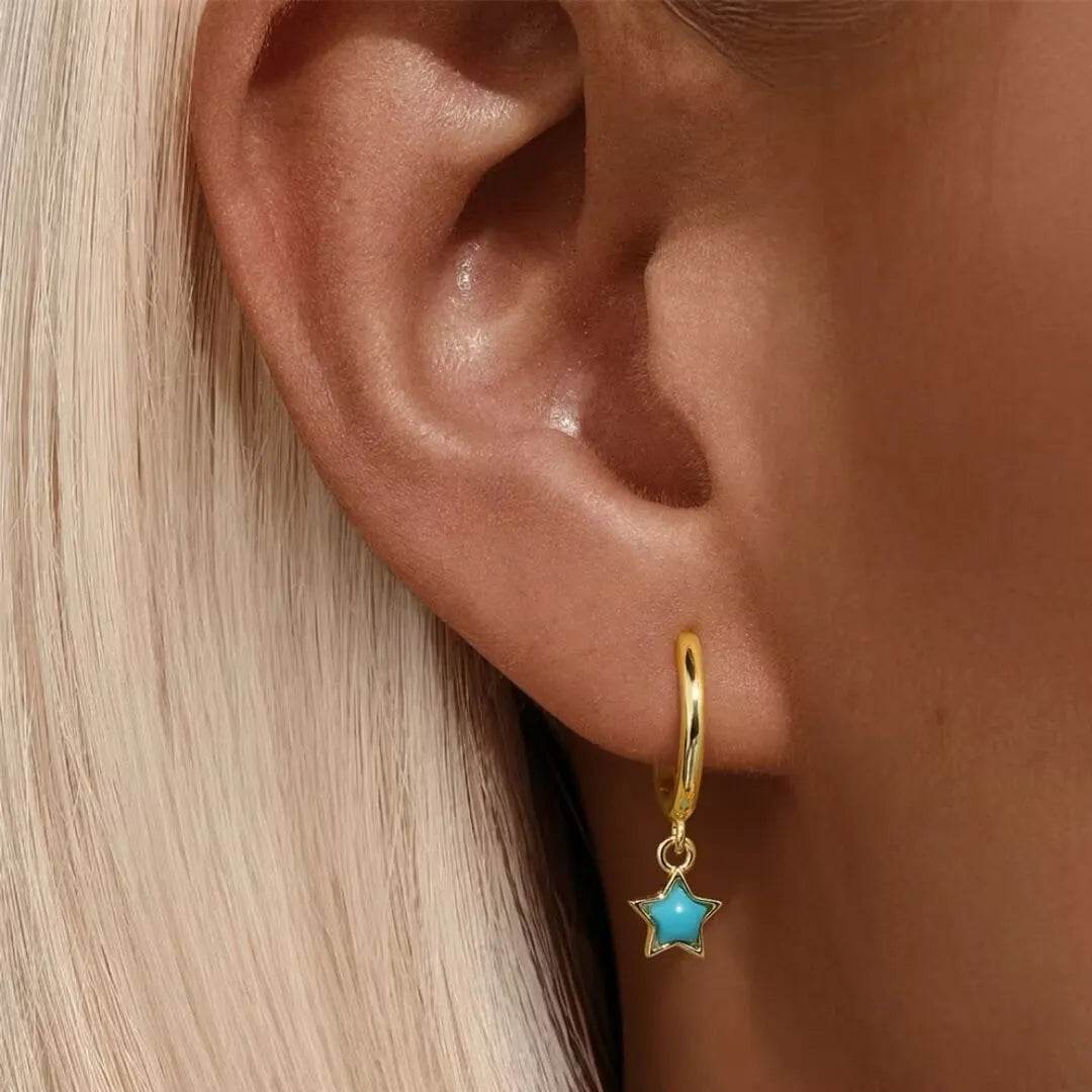 Boucle d'oreille créole plaquée or avec une étoile turquoise suspendue, vue rapprochée sur un lobe d'oreille.