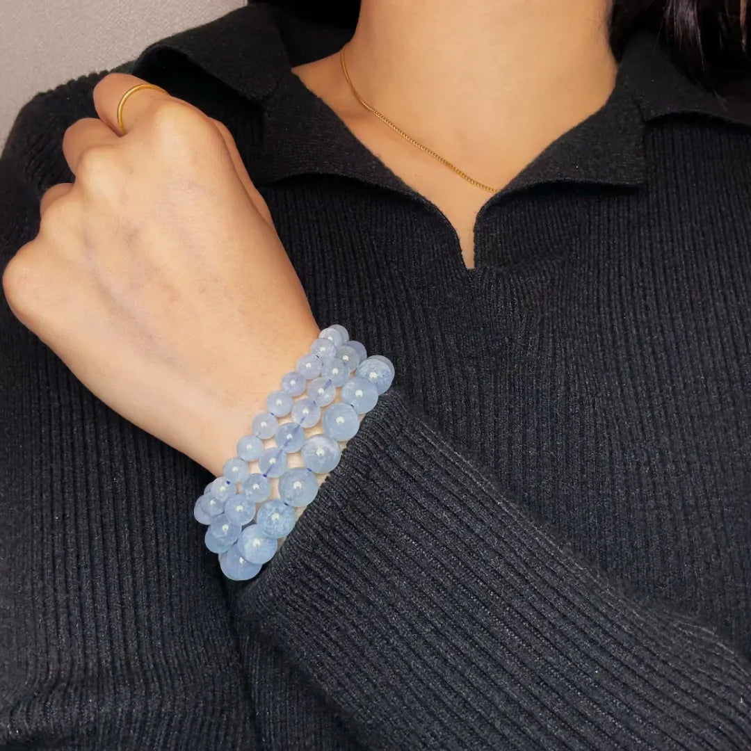 Trois bracelets superposés en pierres d'aigue-marine naturelle "Brise Marine" sur le poignet d'une femme portant un pull noir.