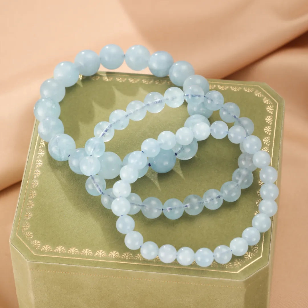 Trois bracelets en perles d'aigue-marine bleu clair sur une boîte verte ornée.