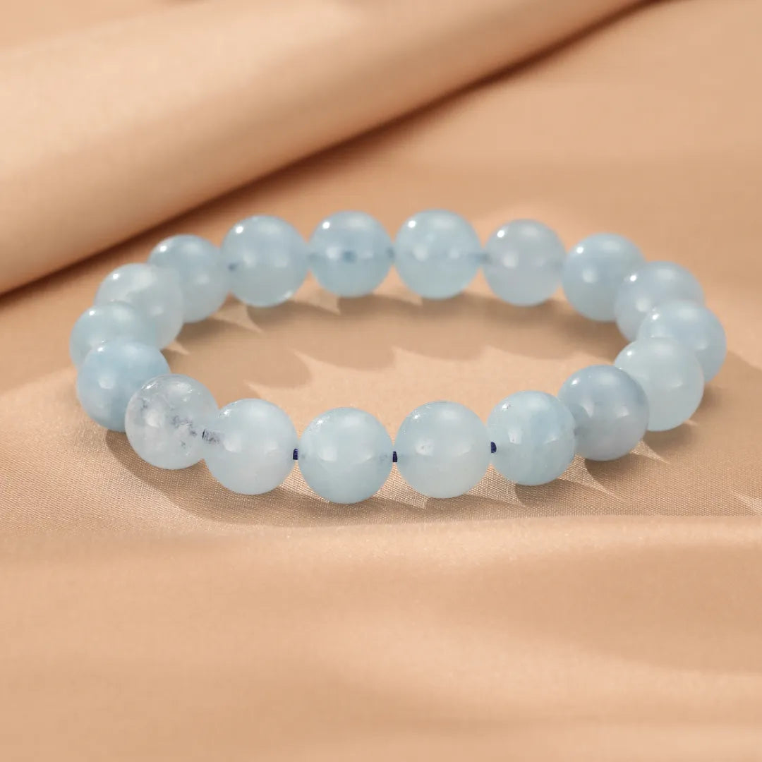 Bracelet "Brise Marine" en aigue-marine, composé de perles rondes bleu ciel légèrement translucides, sur un fond beige satiné.